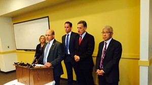Lawrence Miller, senior advisor to Gov. Peter Shumlin, speaks at the press conference on the Vermont Health Connect website. Shumlin and Agency of Human Services Secretary Harry Chen are standing to the right of Miller. Representatives from Optum, the state's vendor managing the project, are also shown.