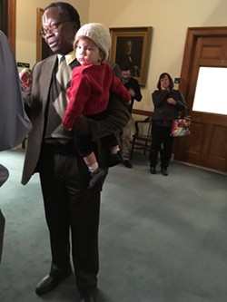 St. Ambroise Azagoh-Kouadio, holding his grandchild, speaks outside the Vermont Supreme Court chambers. - MARK DAVIS