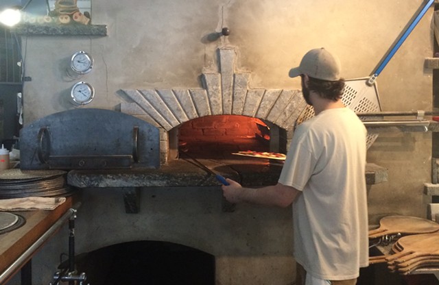 A Folino's staffer puts a pizza in the wood-fired oven - SUZANNE PODHAIZER
