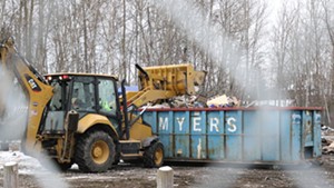 A loader piles debris into a dumpster