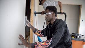 Essex High School senior Mustaf Mohamed uses a surform rasp to make drywall flush with a door frame