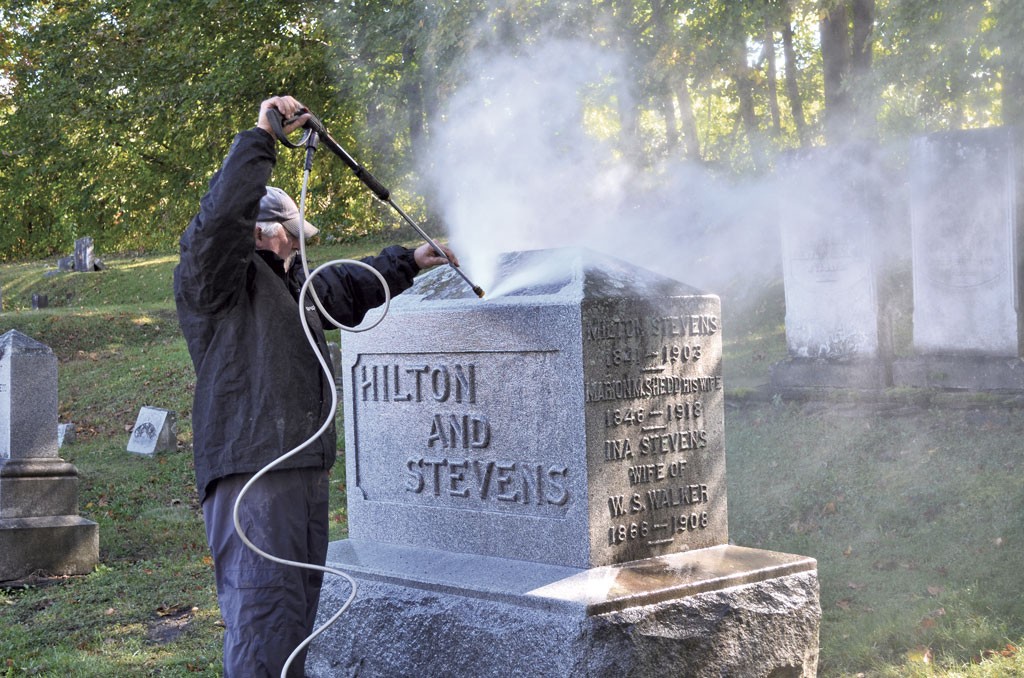 Jim Woodman cleaning mold and lichen off a headstone - ALICIA FREESE